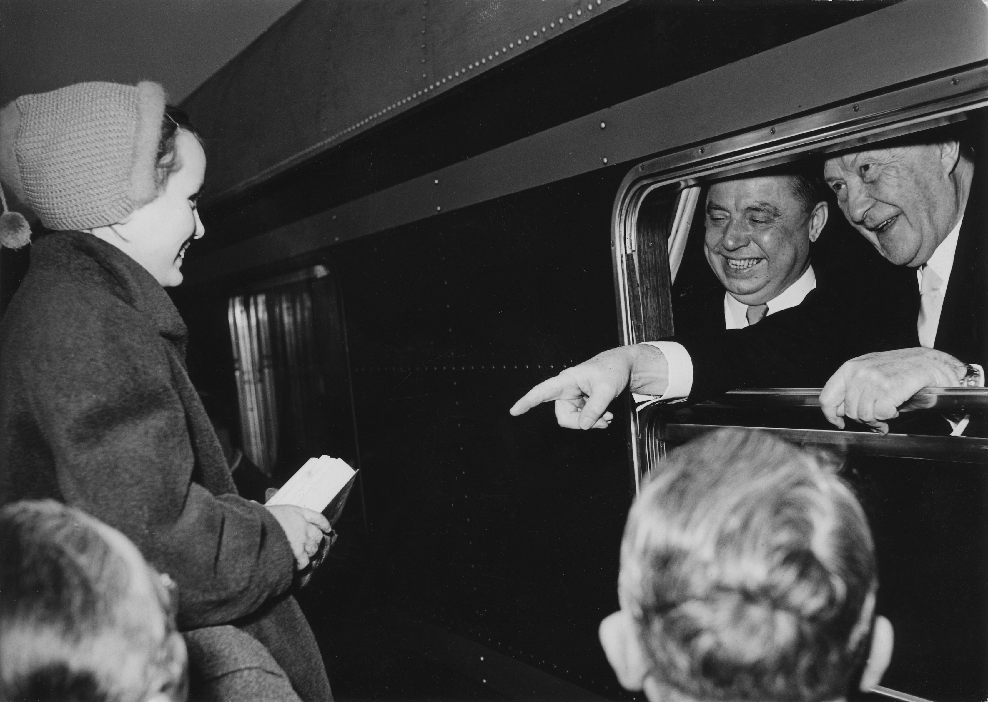 Gut gelaunter Adenauer spricht kurz vor seiner Rückreise aus dem offenen Zugfenster mit den ihn verabschiedenden Bürgern, die den Bahnsteig füllten